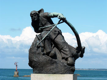 Statue by sea against blue sky