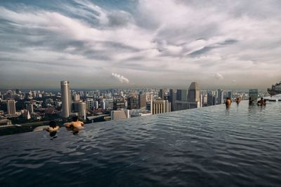 Distant view of city by sea against cloudy sky