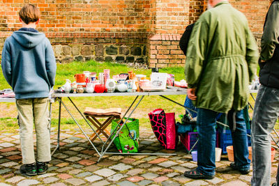 Rear view of people standing on table against brick wall