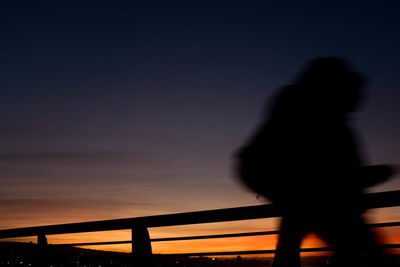 Silhouette woman standing on bridge against sky during sunset