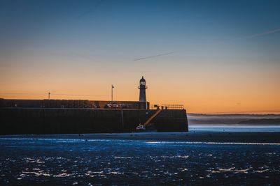 Lighthouse by sea against sky during sunset