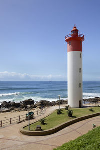 Lighthouse by sea against blue sky