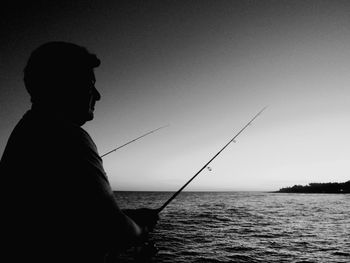 Man fishing in sea against clear sky