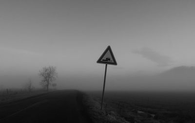 Road sign on field against sky