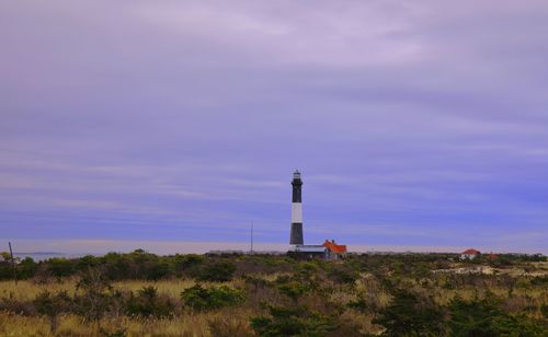 Lighthouse on field by building against sky