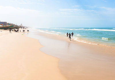 Friends running at beach against sky