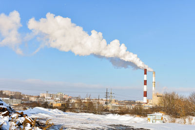 Smoke emitting from factory against sky during winter
