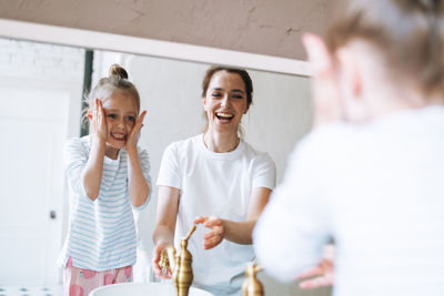 Young woman with little girl daughter in pajamas washing face and hands in morning in bathroom