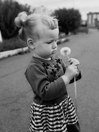 Cute girl holding dandelion standing on road