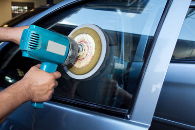 Cropped hands of man polishing car window in auto repair shop