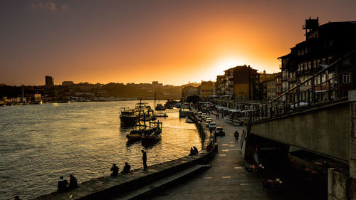 Silhouette buildings by river against sky during sunset