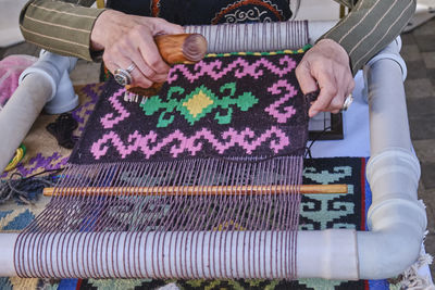 Hands of senior woman weaving a carpet with traditional asian pattern on table handloom