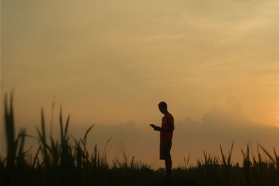 Silhouette man standing on field against sky during sunset