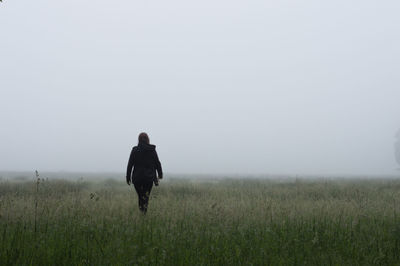 Rear view of woman walking on grassy field in foggy weather