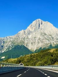 Road leading towards mountains against clear blue sky