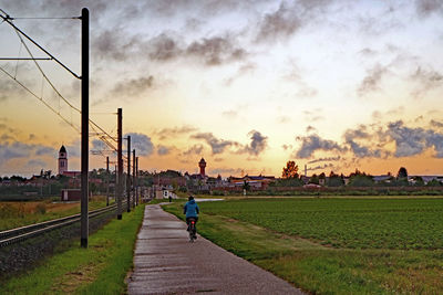 Rear view of man on footpath against sky during sunset