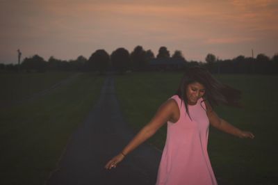 Portrait of young woman standing on field against sky during sunset