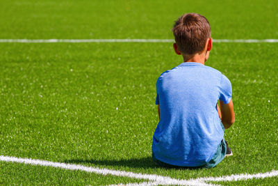 Rear view of boy sitting on soccer field