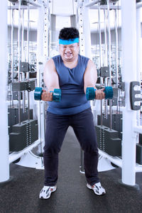 Full length of man holding dumbbell at gym