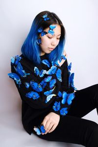 Woman wearing artificial butterflies while sitting against white background