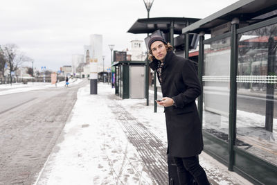 Young man waiting at bus stop in winter