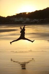 Silhouette person jumping on beach at sunset