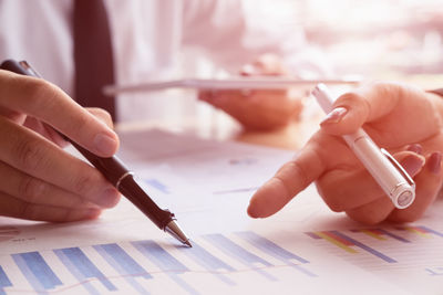 Cropped hands of business people analyzing graphs on desk