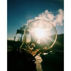 Close-up of hand on glass against sky