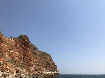 Scenic view of sea and cliff against clear blue sky