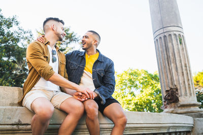 Gay couple talking while sitting against sky