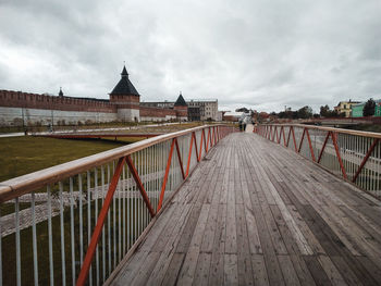 Footbridge in city against cloudy sky