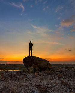 Silhouette man standing on rock at beach against sky during sunset