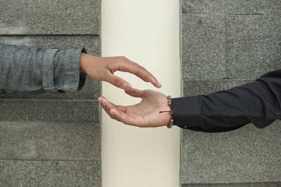 Cropped hands of person shaking hands against wall