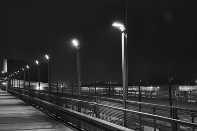 Illuminated railroad tracks by street against sky at night