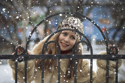 Smiling young woman standing by metal gate during winter