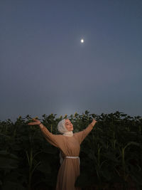 Smiling woman with arms outstretched standing in farm at night