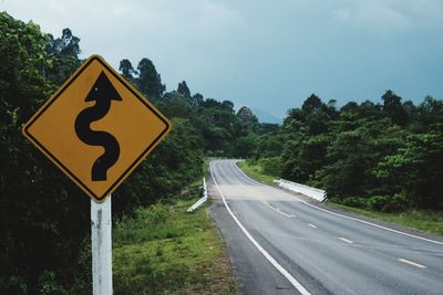 Road sign by street against sky