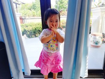 Portrait of cute baby girl standing against window