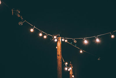 Low angle view of illuminated light bulbs hanging against clear sky