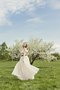 A young blonde in a long white dress poses near a cherry blossom in the garden, a spring landscape.