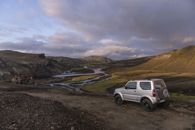 View of car parked on dirt road in valley with river and meanders