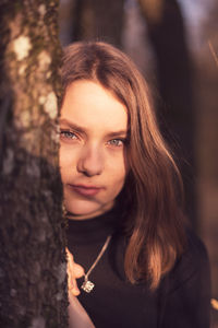 Portrait of young woman by tree trunk