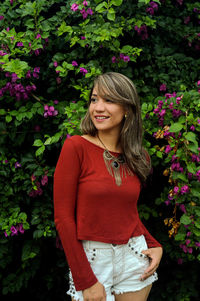 Smiling young woman standing against plants