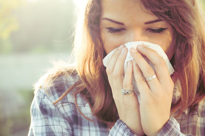 Young woman blowing nose in tissue outdoors