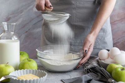 Woman sifting flour through sieve, preparing homemade sweet pie with ripe apples