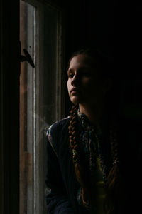 Portrait of woman looking away while standing against window