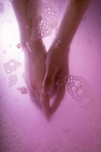 Cropped hands of young woman in pink water