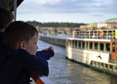 Boy looking at river in city against sky