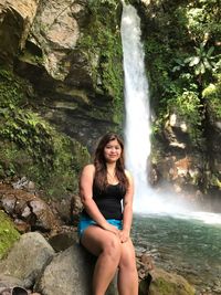 Portrait of young woman sitting on rocks against tuasan falls