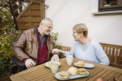 Retired senior man and woman looking at each other while talking at back yard during breakfast